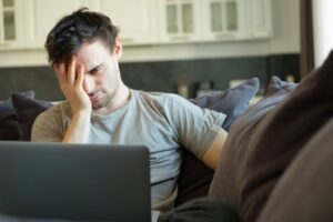 stressed younger man reading bad news on laptop