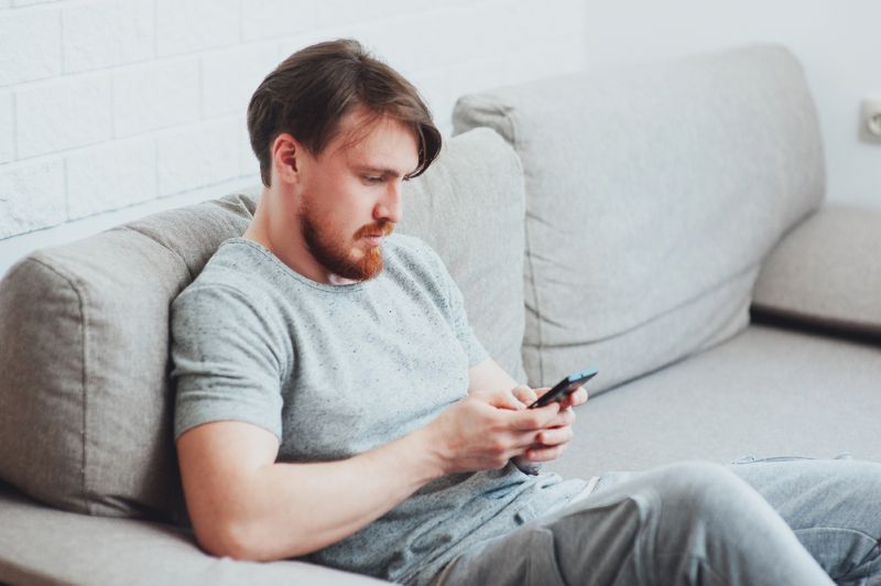 man sitting on his couch using his cell phone