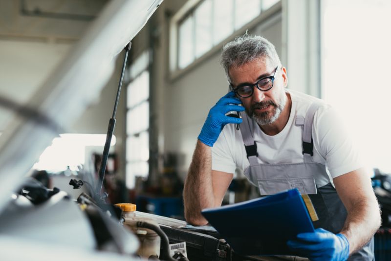 Mechanic working on a car reading paperwork